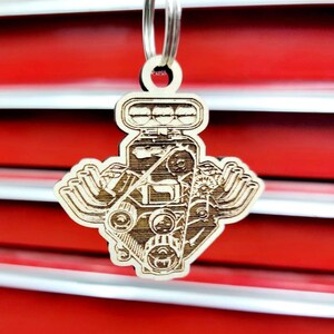 May include: A wooden keychain shaped like a car engine. The keychain is detailed with a realistic depiction of the engine's components, including the pistons, crankshaft, and valve cover. The keychain is a great gift for car enthusiasts.