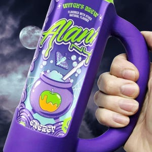 May include: A purple mug with a green rim and handle, featuring the text "Witch's Brew" and "Alan". The mug has a cartoon illustration of a cauldron with an apple and the word "Energy". The background shows a moon and a night sky.