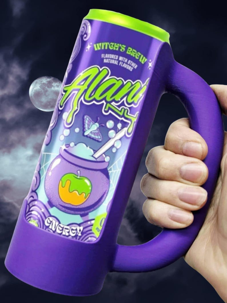 May include: A purple mug with a green rim and handle, featuring the text "Witch's Brew" and "Alan". The mug has a cartoon illustration of a cauldron with an apple and the word "Energy". The background shows a moon and a night sky.