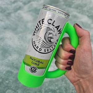May include: A can of White Claw Hard Seltzer Natural Lime in a bright green holder. The can is silver with black and white text and a wave graphic. The holder has a handle for easy carrying.