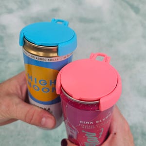 May include: Two beverage cans with colorful lids. One can is blue and yellow with the text "HIGH NOON". The other can is pink with the text "PINK SLUSH". Both cans have a matching colored lid with a handle.