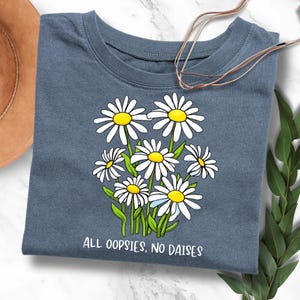 Könnte beinhalten: Ein blaues T-Shirt mit einem weißen Gänseblümchen-Druck und dem Text "All oopsies, no daisies".