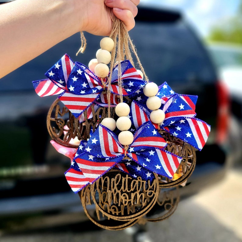 May include: Wooden ornaments with red, white, and blue ribbon bows and the words "Military Mom" and "Support Our Troops". The ornaments are strung together with wooden beads.