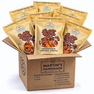May include: A cardboard shipping box filled with multiple tan bags of Martin's Handmade Buffalo Wing Sourdough Pretzel Pieces. Each bag features the text Food isn't made how it used to be—ours is, and a net weight of 6 oz printed on the front.