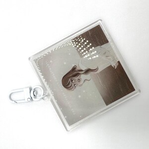 May include: A clear acrylic keychain with a silver clasp. The square pendant features a sepia-toned illustration of a woman with long hair, with the text "THE TORMENTED POETS DEPARTMENT" around the border.