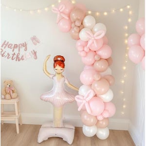 May include: A party scene with a pink and white balloon arch, a ballerina-shaped balloon, and scattered pink balloons. The words "Happy Birthday" are displayed on the wall, creating a celebratory atmosphere.