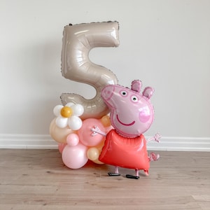 Könnte beinhalten: Ein großer beiger Ballon in Form der Zahl 5 mit einem Peppa Pig Ballon davor. Der Peppa Pig Ballon ist rosa mit einem roten Kleid und schwarzen Schuhen. Um die Basis des Zahlenballons herum befinden sich kleinere Ballons in Rosa, Pfirsich und Creme.