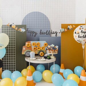 K&ouml;nnte beinhalten: Eine festliche Geburtstagsfeier mit Luftballons, einem Spielzeugbagger und einem Tisch mit Donuts und Cupcakes. Die Szene umfasst ein Banner mit der Aufschrift "Happy Birthday" und einen Ballon mit der gleichen Aufschrift. Das Farbschema umfasst Gelb, Blau und Orange.