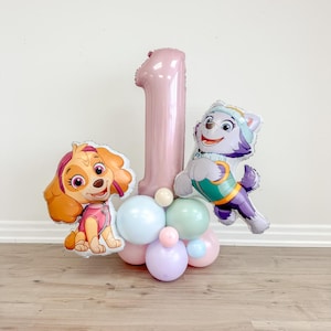 May include: A pink number one balloon with a Paw Patrol character balloon on each side. The balloons are surrounded by pastel colored balloons.