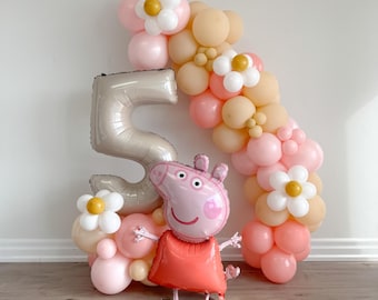 May include: A pink Peppa Pig balloon character stands in front of a balloon arch made of pink, peach, and white balloons. The arch is shaped like the number 5, and there are white flowers with yellow centers on the arch.