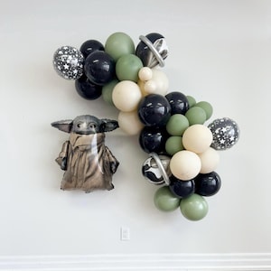May include: A green, black, and cream balloon arch with a silver and black star-shaped balloon. A brown and green character balloon is in the foreground.