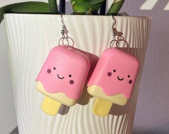May include: A pair of pink and yellow popsicle earrings with a smiling face. The earrings are made of polymer clay and have silver hooks.