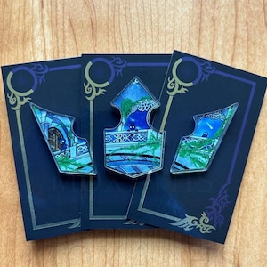 Op de afbeelding: Drie blauwe en groene glazen pinnen met een glas-in-loodontwerp. De pinnen zijn pijlvormig en tonen een nachtelijke hemel met sterren en een klein figuurtje in het midden.