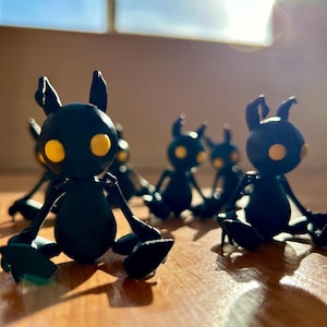 May include: A group of five black figurines with yellow eyes. The figurines are sitting on a wooden surface. The figurines are in a variety of poses.
