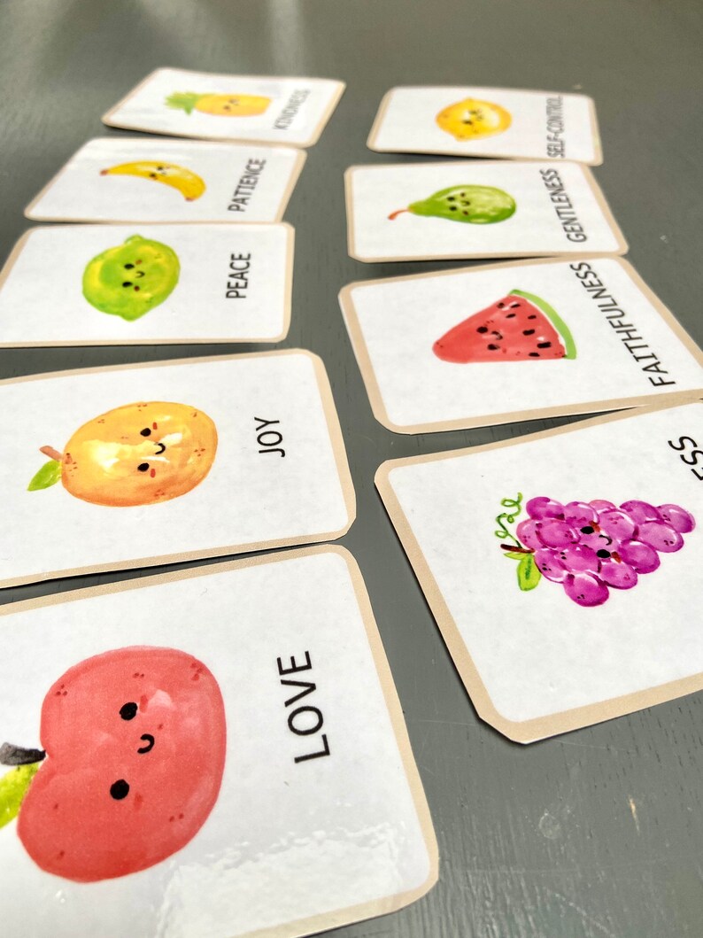 Pode incluir: Um conjunto de cartas coloridas com ilustra&ccedil;&otilde;es de frutas e palavras como "amor", "alegria", "paz", "paci&ecirc;ncia", "bondade", "fidelidade", "mansid&atilde;o" e "autocontrole".