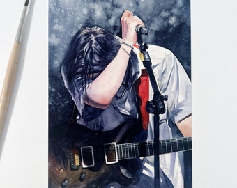 May include: Watercolour painting of a musician performing on stage. The figure is bent over, holding a microphone and a black electric guitar. The musician wears a white shirt with a red strap and has long black hair.