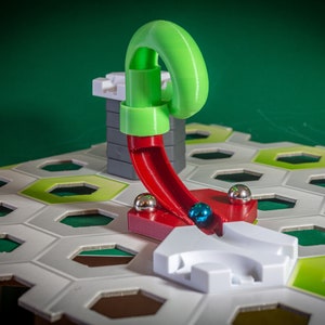 Puede incluir: Un juego de canicas verde y rojo con una rampa de pl&aacute;stico verde y una pista de pl&aacute;stico rojo. La pista est&aacute; unida a una base de pl&aacute;stico gris. Una canica azul rueda por la pista.