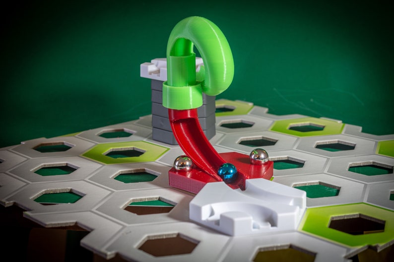 Puede incluir: Un juego de canicas verde y rojo con una rampa de pl&aacute;stico verde y una pista de pl&aacute;stico rojo. La pista est&aacute; unida a una base de pl&aacute;stico gris. Una canica azul rueda por la pista.