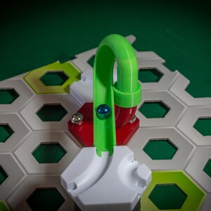 Puede incluir: Una pieza de pista de pl&aacute;stico verde para un juego de carrera de canicas. La pista es curva y tiene una base roja. Una canica azul rueda por la pista.