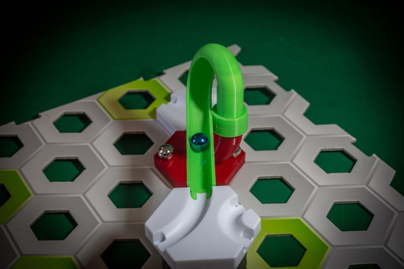 Puede incluir: Una pieza de pista de pl&aacute;stico verde para un juego de carrera de canicas. La pista es curva y tiene una base roja. Una canica azul rueda por la pista.