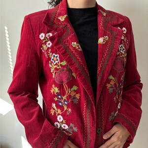 May include: A red corduroy blazer with colourful floral embroidery. The embroidery features white, purple, and orange flowers with green leaves. The blazer has a notched collar and a single button fastening.