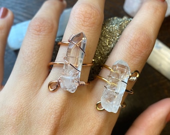 May include: Two clear quartz crystal rings wrapped in copper wire. The rings are on a person's fingers.