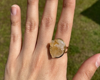 May include: A gold ring with a large, raw, light brown crystal stone.