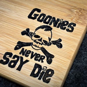 Peut inclure: Une planche &agrave; d&eacute;couper en bois avec un motif noir et blanc repr&eacute;sentant un cr&acirc;ne et des os crois&eacute;s, les mots "Goonies Never Say Die" et un motif de grain de bambou.