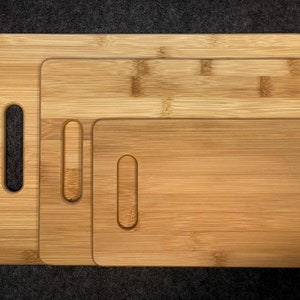 Peut inclure: Trois planches &agrave; d&eacute;couper en bois de diff&eacute;rentes tailles, toutes en bambou brun clair avec un motif de grain naturel. Chaque planche a une poign&eacute;e d&eacute;coup&eacute;e sur le c&ocirc;t&eacute;.