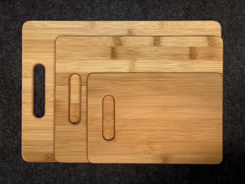 Peut inclure: Trois planches &agrave; d&eacute;couper en bois de diff&eacute;rentes tailles, toutes en bambou brun clair avec un motif de grain naturel. Chaque planche a une poign&eacute;e d&eacute;coup&eacute;e sur le c&ocirc;t&eacute;.