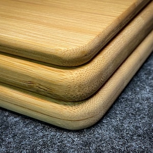 Peut inclure: Trois planches &agrave; d&eacute;couper en bambou naturel empil&eacute;es les unes sur les autres. Les planches ont des bords arrondis et une surface lisse de couleur brun clair.