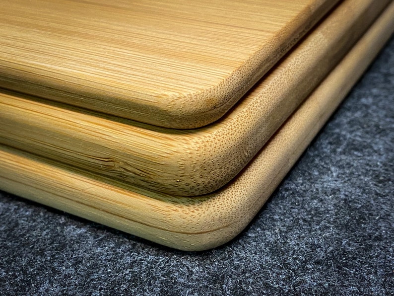 Peut inclure: Trois planches &agrave; d&eacute;couper en bambou naturel empil&eacute;es les unes sur les autres. Les planches ont des bords arrondis et une surface lisse de couleur brun clair.