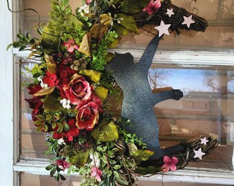 May include: A black metal cat silhouette holding a star, with a wreath of red, pink and white flowers around it.