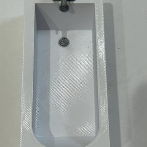 May include: A miniature white bathtub with a textured interior and a silver faucet. The tub has a rectangular shape with rounded corners and a drain in the center. The faucet is a simple, two-handle design.
