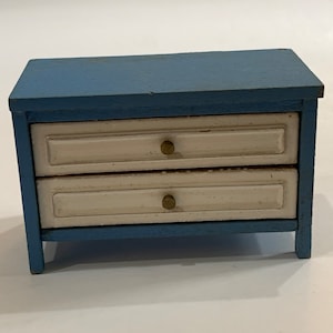 May include: A small blue wooden dresser with two drawers. The drawers have white fronts and brass knobs.