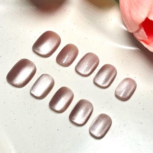Può includere: Un set di dieci unghie finte in un colore oro rosa scintillante e perlescente. Le unghie, di forma ovale, sono disposte in fila ordinata, mostrando una finitura lucida. Le unghie sono un prodotto di bellezza.