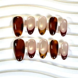 May include: A collection of ten oval false nails. The designs include a tortoiseshell pattern and a French tip style with a nude base and dark red tips. The nails have a glossy finish, suggesting a professional application. The nails are well-manicured.