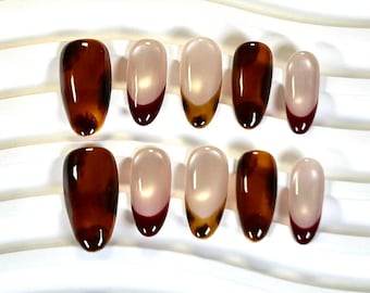 Puede incluir: Un juego de diez uñas postizas con forma de almendra. El diseño presenta un acabado brillante con una combinación de patrones de carey marrón oscuro y puntas estilo francés con una base color nude y bordes marrón oscuro en varias uñas.