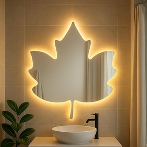 Peut inclure: Salle de bain moderne avec un miroir en forme de feuille d'érable éclairé par des LED chaudes. Elle comprend un lavabo blanc, un robinet noir et un meuble-vasque en bois clair. Une plante en pot ajoute une touche de verdure.