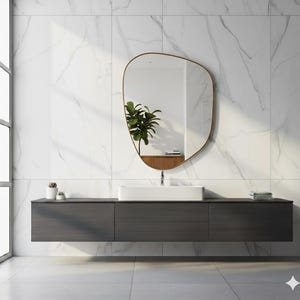 Könnte beinhalten: Ein modernes Badezimmer mit einem großen, unregelmäßig geformten Spiegel mit goldenem Rahmen. Darunter befindet sich ein dunkelgrauer, schwebender Waschtisch mit einem weißen, rechteckigen Waschbecken. Der Hintergrund ist weißer Marmorfliesen, und links ist ein Fenster zu sehen.