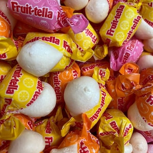 May include: A close-up of a variety of colorful candy wrapped in foil. The candy is in the shape of a sphere and is covered in a white, sugary coating. The candy wrappers feature the text "Fruit-tella" in a variety of colors.