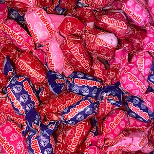 May include: A close-up of a variety of Fruit-tella candies wrapped in colorful foil. The candies are in a variety of flavors, including strawberry, raspberry, and blueberry. The candies are all individually wrapped and ready to be enjoyed.