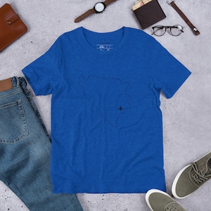 May include: A royal blue short-sleeved t-shirt featuring a thin black outline of the map of Bosnia and Herzegovina centered on the chest. A small black fleur-de-lis symbol is positioned within the map outline toward the lower right side.