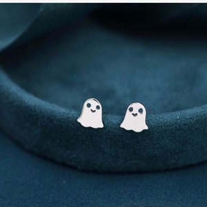 Puede incluir: Un par de pendientes de botón de plata en forma de fantasma. Los fantasmas tienen una cara sonriente simple.