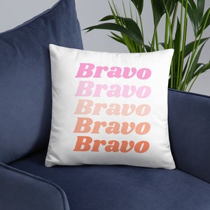 May include: White cushion with the word "Bravo" repeated five times in a gradient of pink and orange.