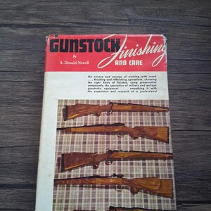 May include: A book titled "Gunstock Finishing and Care" by A. Donald Newell. The cover is red and white with the title in large, stylized letters. The cover features images of wooden gunstocks.