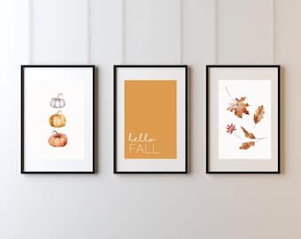 May include: Three framed art prints with black frames. One print features watercolor pumpkins, another has the text "hello FALL" on an orange background, and the third displays autumn leaves.