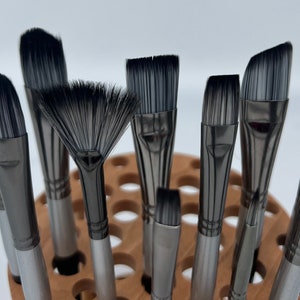 A wooden rotating paintbrush holder with a circular base and a cylindrical center. The holder has many holes to hold paintbrushes. The holder is filled with a variety of paintbrushes with different colored handles and bristles.