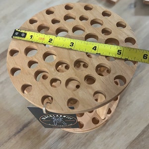 A wooden rotating paintbrush holder with a circular base and a cylindrical center. The holder has many holes to hold paintbrushes. The holder is filled with a variety of paintbrushes with different colored handles and bristles.