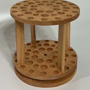 A wooden rotating paintbrush holder with a circular base and a cylindrical center. The holder has many holes to hold paintbrushes. The holder is filled with a variety of paintbrushes with different colored handles and bristles.